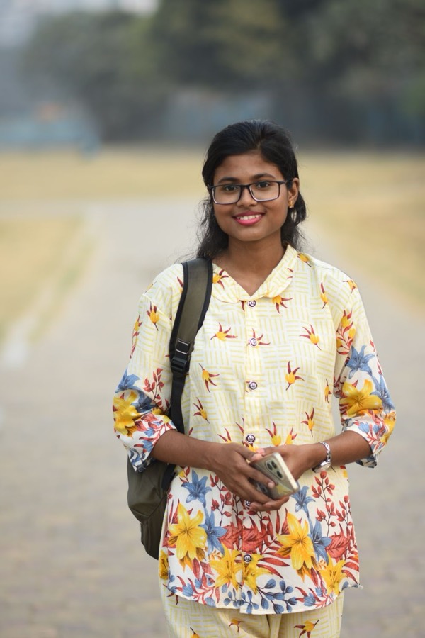 A smiling student in glasses holding books, with a backpack over one shoulder