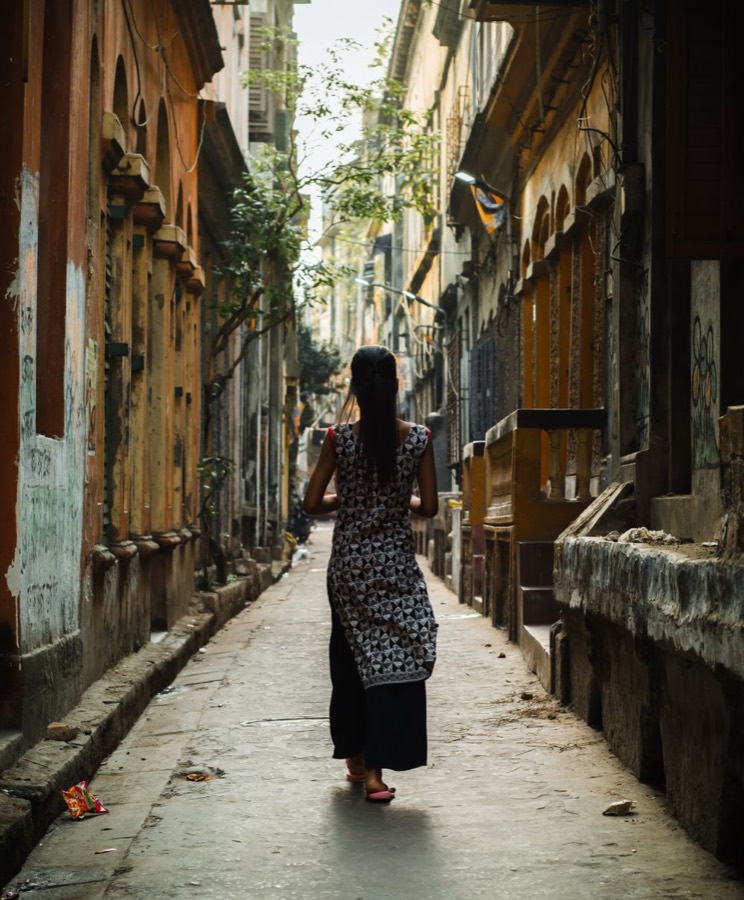 A young woman seen from behind, walking alone down a narrow lane